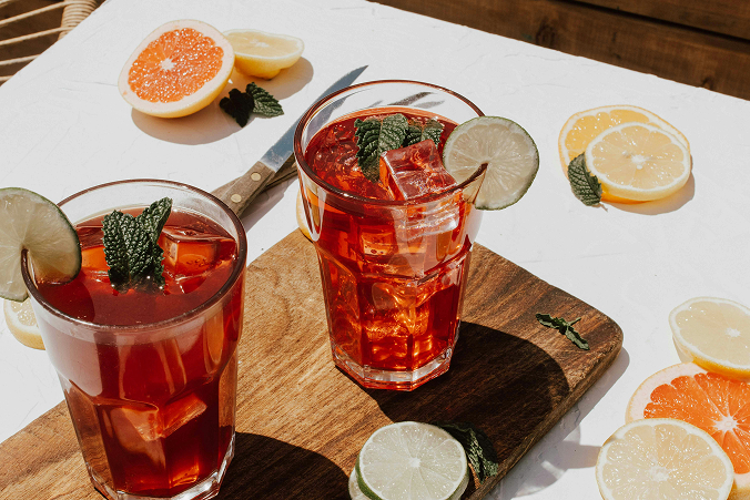 Two highball cocktails garnished with mint on a chopping board surrounded by citrus slices